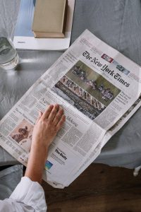 A person reading an open newspaper on a gray desk.