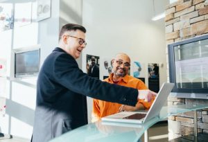 Two men with glasses looking at a laptop, with one pointing at it.